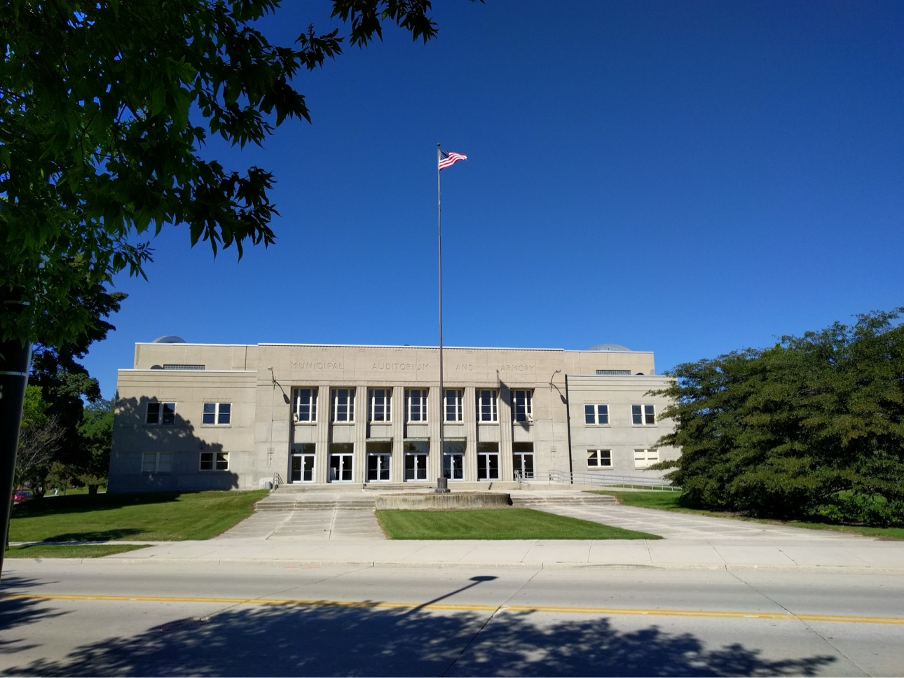 Modern color photo of the Sheboygan Municipal Auditorium and Armory exterior, flag pole, blue sky
