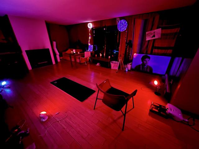 his apartment bathed in red/purple light, yoga mat, fairy lights, TV