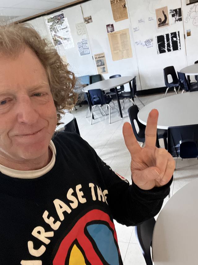 Mike in a classroom, "INCREASE THE PEACE" shirt, peace sign (his teaching years