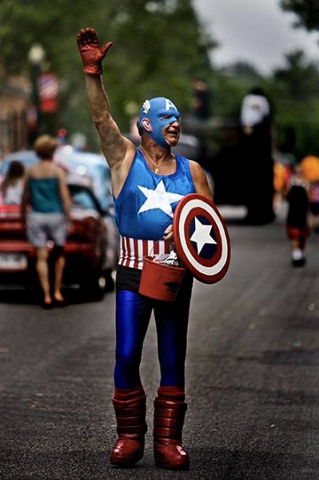 man in a Captain America costume marching with his shield and candy bucket (parade set
