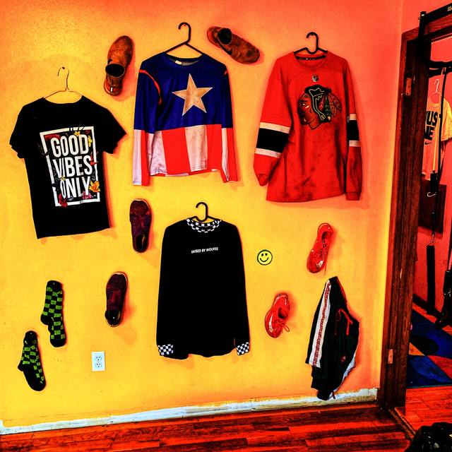 shirt/shoe wall on orange: "GOOD VIBES ONLY," Blackhawks jersey, "RAISED BY WOLVES"