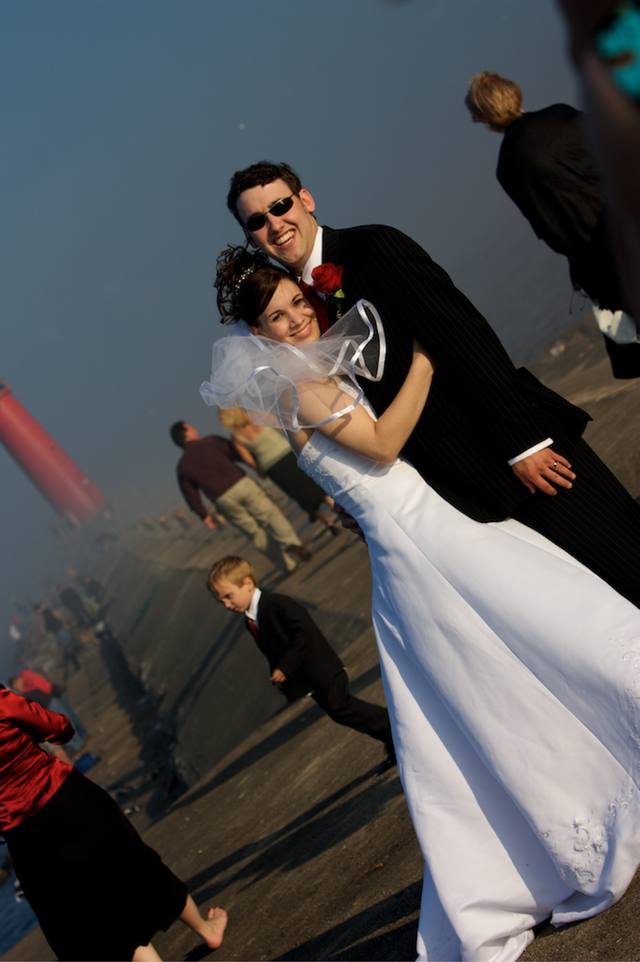 The couple embracing on the pier, red lighthouse behind, the boy wandering the frame