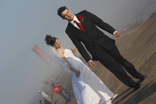 The couple mid-stride on the breakwater, fishermen in the mist