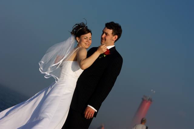 Bride straightening the boutonniere, lighthouse over his shoulder